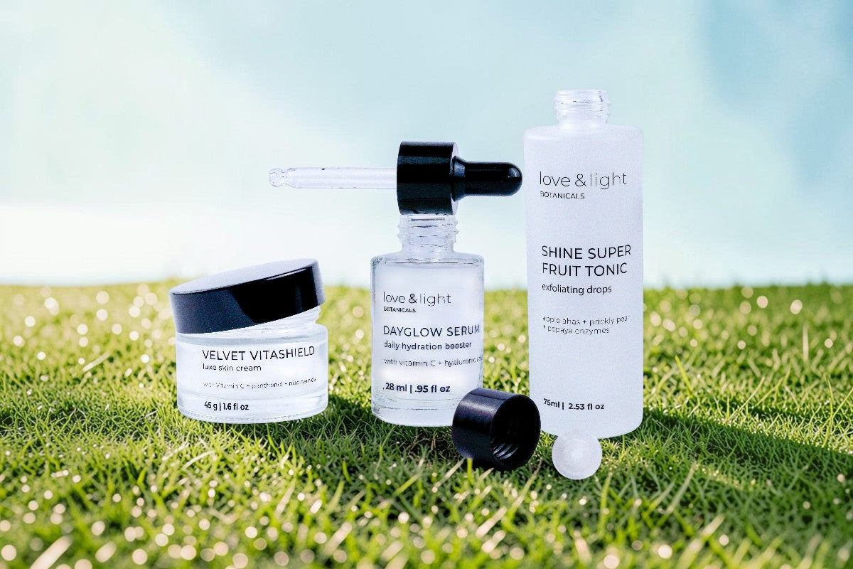 Refillable skincare products from the brand love & light are arranged on a green grassy surface with a soft blue sky background.