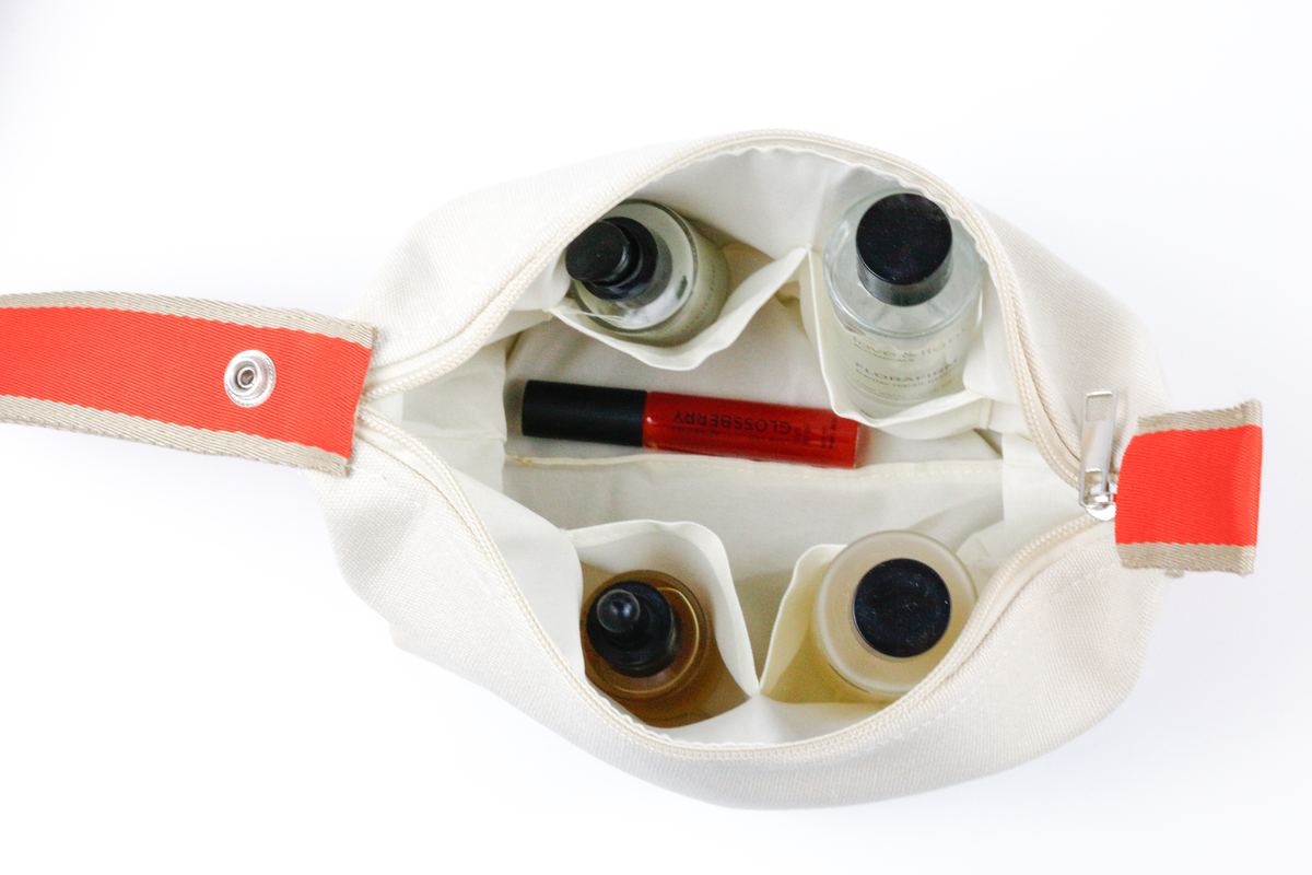 Top view of an open white cosmetic case with four bottle sleeves holding skincare + Glossberry lip oil