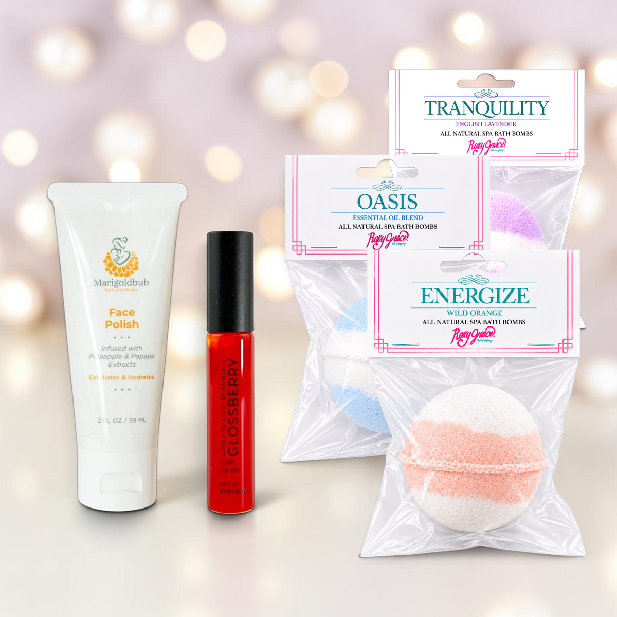 Gift set items including Marigoldbub Face Polish, Glossberry lip oil and three packaged Roxy Grace bath bombs on a shimmery holiday background.