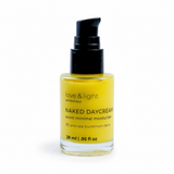 A bottle of Love & Light Botanicals Naked Daycream, a scent minimal moisturizer in a clear glass bottle showing yellow cream inside, with a black pump dispenser, on a white background.